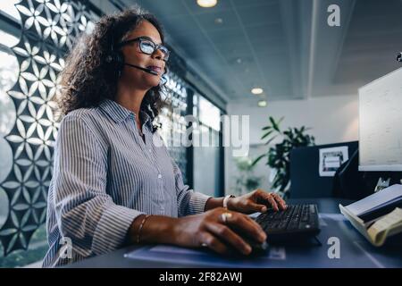 Shot of a woman using a headset and computer in a modern office. Customer service agent working at  her desk. Stock Photo