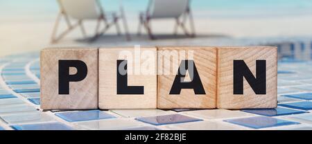 Plan word made with building blocks on relaxed beach background. Sun umbrella and sea. Business investment concept. Stock Photo