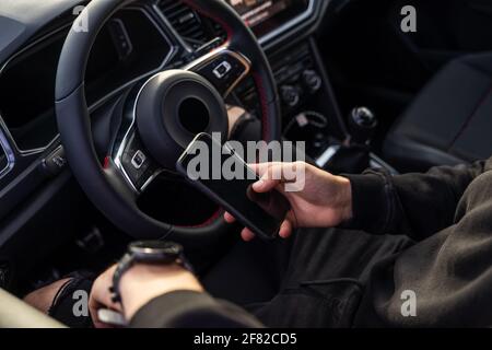 Unrecognisable man sitting in the pilot's seat using a mobile phone, wearing dark, modern clothes, holding the phone in one hand and a smart watch in Stock Photo