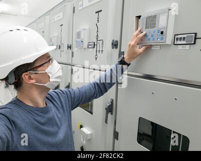 Young engineer working in electrical substation wearing a face mask. Stock Photo