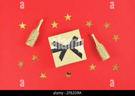Golden gift box with black bow, small Champagne bottles and stars on red background Stock Photo