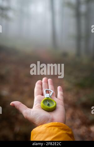 Make decision which way to go from misty forest. Lost traveler holding compass in her hand. Woman hiking in nature Stock Photo