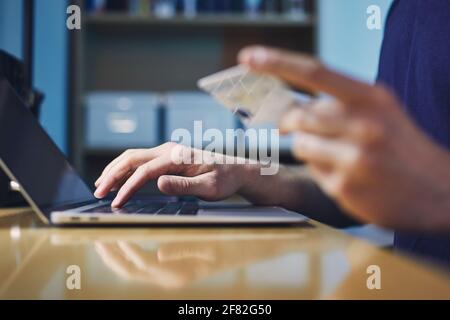 Close-up hands of person during online shooping. Young man holding credit card and using laptop. Stock Photo