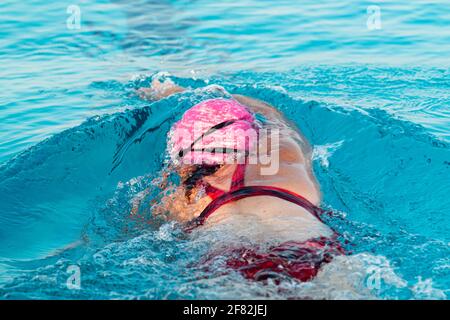 Rear view of a female swimmer in a pool pushing off of the wall splashing in the water while triathlon training. Stock Photo