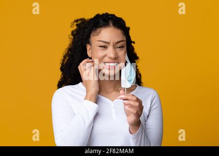 Itchy Skin. Annoyed African American Woman Scratching Face After Wearing Medical Mask Stock Photo