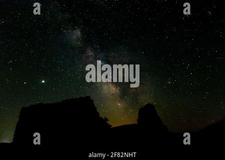 An eerie scenery of a silhouette of a cliff on a starry night sky with glowing Milky way Stock Photo