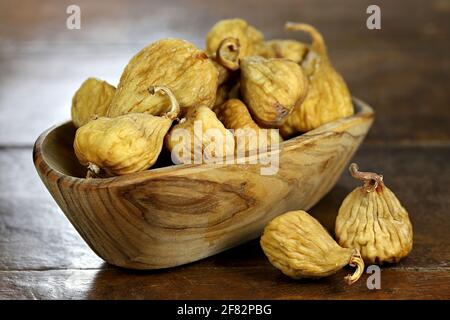 dried wild figs in a bowl made of olive wood isolated on rustic wooden table Stock Photo
