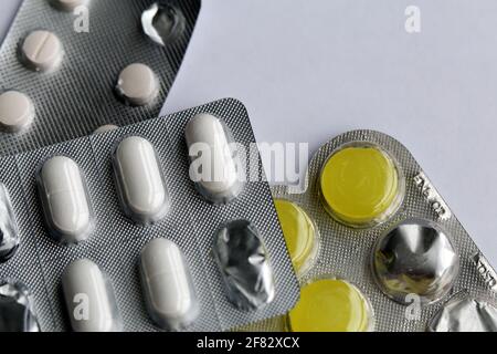 Plenty of different medications - pills for sore throat, painkillers and more photographed on a white table. Good drugs for cold and flu. Closeup. Stock Photo