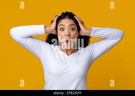 Oh No. Shocked african american lady touching head and looking at camera Stock Photo