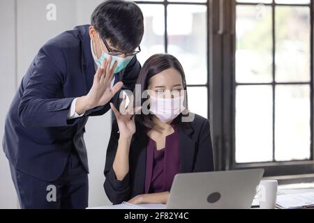 businessman and women wearing face masks while using laptop and greeting someone during video call in the office. conference with work team amid COVID Stock Photo