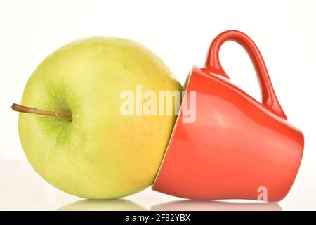 One bright green organic, ripe, juicy, tasty Granny Smith apple, close-up, with a red ceramic cup. The background is white. Stock Photo