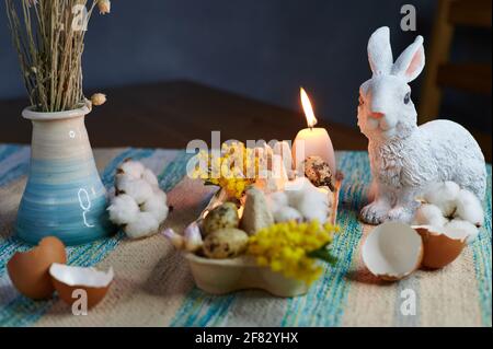 decor in an egg box with burning candles, hare and mimosa Stock Photo