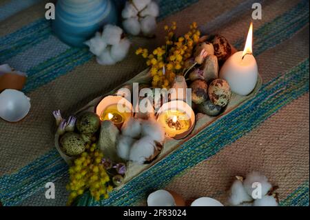 Easter decor in an egg box with burning candles and dried flowers Stock Photo