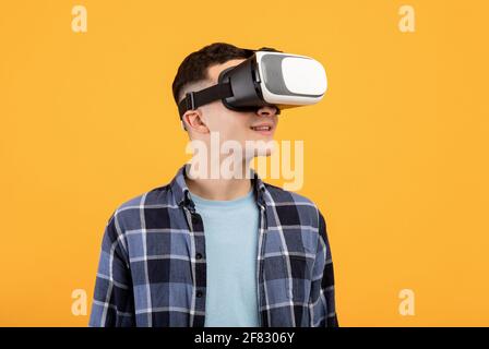 Cool guy in VR headset exploring cyberspace, using virtual reality for entertainment or studies on orange background Stock Photo