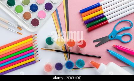 Overhead view of colorful school art supplies with colored pencils, markers, paint and paper on a white table Stock Photo