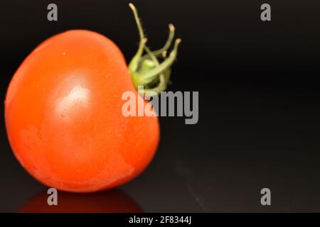 One ripe, bright red, organic, tasty cocktail tomato, close-up, on a black background. Stock Photo