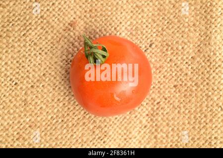 One ripe, bright red, organic, delicious cocktail tomato on jute fabric. Stock Photo