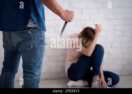 Victim afraid of tyrant, frightened lady covers her face with hands and sits on floor Stock Photo