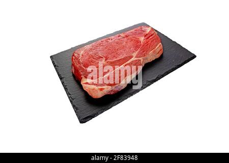 Juicy raw meat cut. Beef entrecote slice on the black textured slate plate isolated on white. Stock Photo