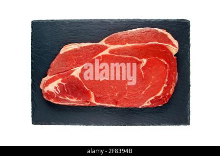Juicy raw meat cut. Beef entrecote slice on the black textured slate plate isolated on white top view. Stock Photo