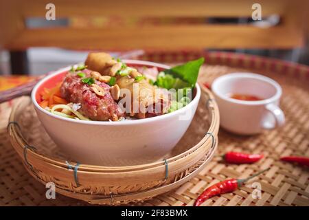 Vietnamese dish of cold rice-vermicelli noodle topped with grilled pork, fresh herbs, fresh salad, and spring rolls Stock Photo