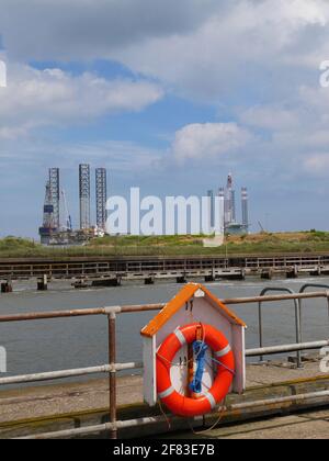 Brightly Coloured Life-belt on Gorleston's South Pier, beside The River Yare's entrance to The Port of Great Yarmouth, with North Sea Rigs. Stock Photo