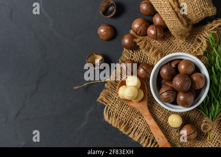 Dry Roasted Macadamia Nut in wood spoon and on black background, Macadamia nuts are loaded with flavonoids and tocotrienols and rich in heart-healthy Stock Photo