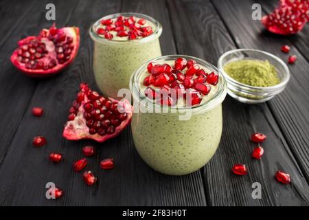 Pudding with chia, matcha tea and pomegranate seeds in the two glass jars on the black wooden background. Closeup. Stock Photo