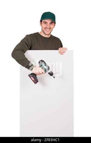 Smiling man with a screwdriver or electric drill in his hand, stands behind a white panel. Renovation worker before installing interior finish plate o Stock Photo