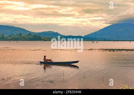 Man on small wooden boat floating on the lake in the morning scenery Stock Photo