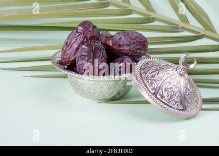 Religious Islamic festival and holy month of Ramadan, EID KAREEM, concept: A silver bowl with dried date fruits. Palm leaves on green background Stock Photo