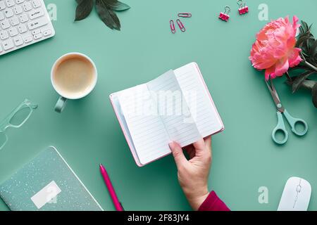 Save the date invitation card design. Hand with pen, home office. Text space, copy-space in notebook..Pink peony flowers on green mint table. Coffee, Stock Photo