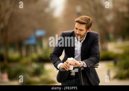 Handsome young businessman drinking take away coffee cup on electric scooter Stock Photo