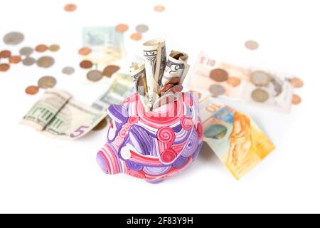 Kids piggy bank stuffed with paper money and coins on top of defocused and abstract international currency. Concept for saving money early, finance an Stock Photo