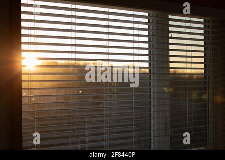 focus on the blinds of a window with the sun shining behind Stock Photo