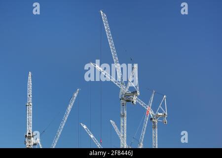 White construction cranes against the blue sky in a construction site in London, UK Stock Photo
