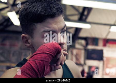 Young boxer with red hand wraps preparing for boxing practice in boxing club Stock Photo