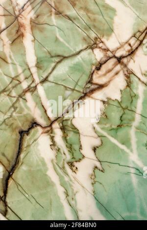 Unusual texture of old green marble with brown and beige spots, diagonal cracks and scratches. Polished surface. Vertical image. Stock Photo