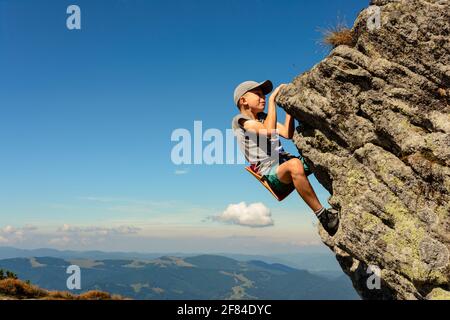 The boy is engaged in mountaineering, a child climbing a rocky mountain, a brave boy.2020 Stock Photo