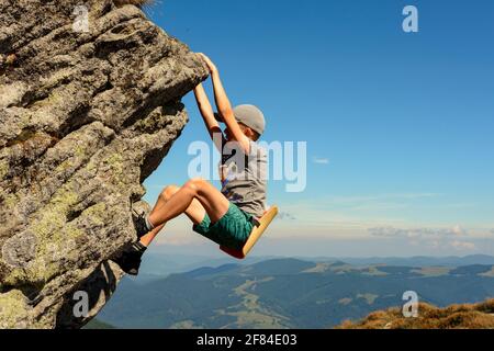 The boy is engaged in mountaineering, a child climbing a rocky mountain, a brave boy.2020 Stock Photo