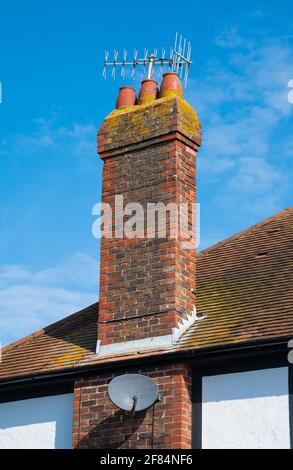 Tall red brick chimney with 3 chimney pots and with TV aerial and satellite dish, on a 20th century house in England, UK. Stock Photo