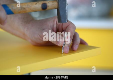 Close-up of foremans hand hammer nail into yellow door Stock Photo