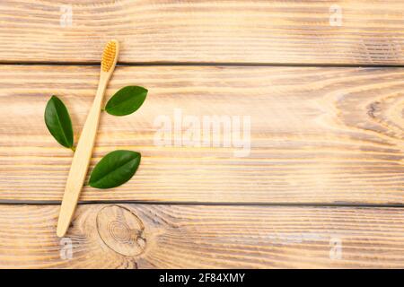 Natural eco friendly bamboo toothbrush with green tree leaves on a wooden background. Choose a wooden toothbrush. Recycling concept, no waste, no plas Stock Photo