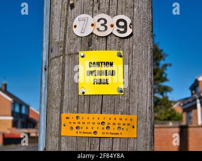 A yellow sign fixed to a wooden telegraph pole warns that optic fibre lines are overhead. Taken on a sunny day in an urban area of north west England. Stock Photo