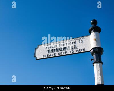 Isolated against a clear blue sky, a white metal sign shows the way on a footpath from Storeton to Thingwall on Wirral in the UK Stock Photo
