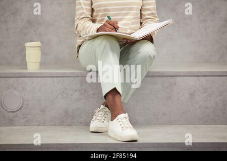Graphic low section shot of unrecognizable African-American woman studying alone in modern school lounge and writing in notebook, copy space Stock Photo