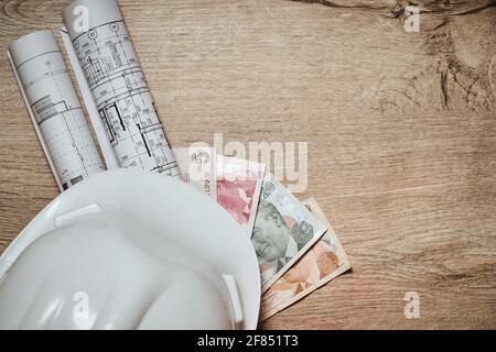 Rolled drawings, white hardhat and turkish lira at wooden table Stock Photo