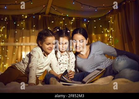 Mother with daughters children reading book spending time in home tent Stock Photo