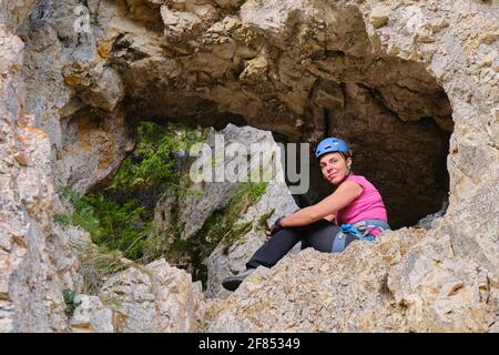 Woman sits in a rock grotto on a via ferrata route located at Piatra Soimilor, Harghita county, Romania. Adventure, tourism, summer. Stock Photo