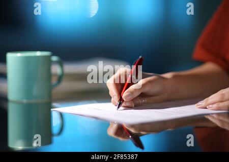 Close up of a woman hand filling out paper form in the night at home Stock Photo